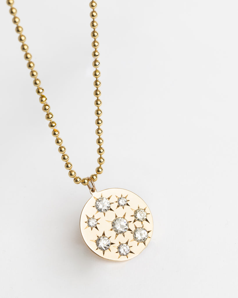 Gold necklace with a round pendant featuring star-shaped cutout designs on a light gray background
