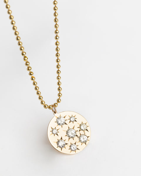 Gold necklace with a round pendant featuring star-shaped cutout designs on a light gray background