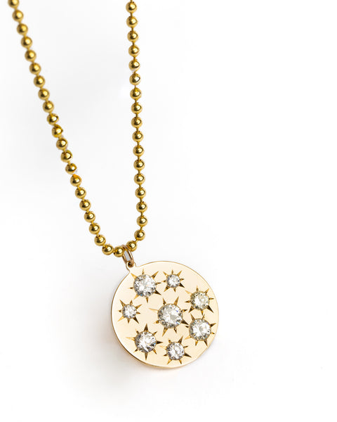Gold necklace with a round pendant featuring star-shaped cut stones on a white background